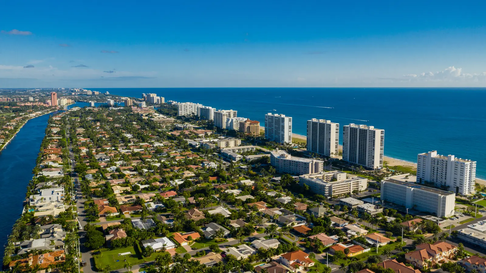 Aerial view of a South Florida coastal strip, with the Intracoastal Waterway on one side, single-family neighbourhoods and oceanfront condominium towers in the middle, and the Atlantic Ocean on the other.