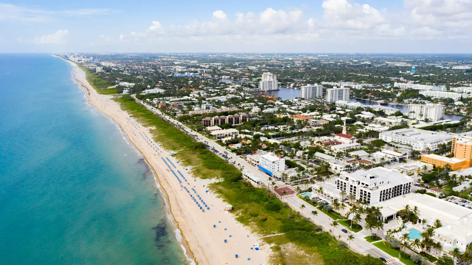 Aerial view along a South Florida beach, showing a long coastal strip, blue water and a populated shoreline.