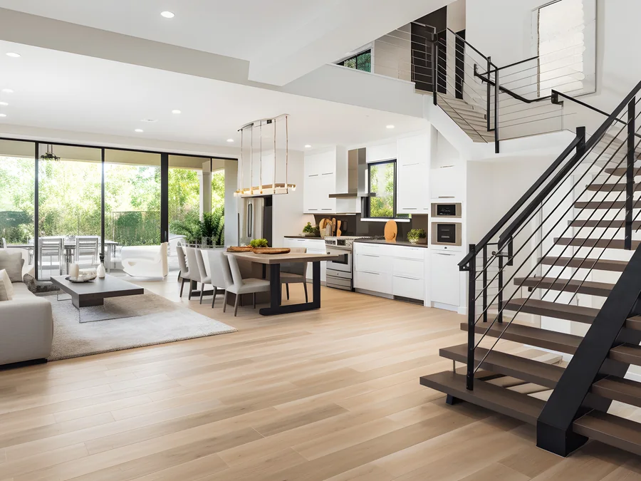 Open-plan modern living room with a floating staircase, an open kitchen and floor-to-ceiling glass sliders onto a garden.