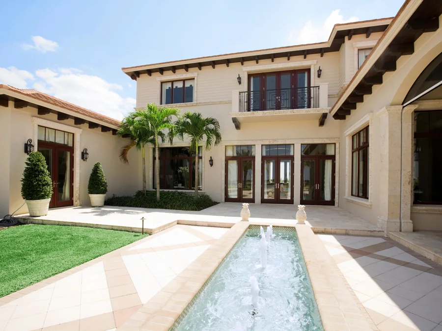 Rear elevation of a Mediterranean-style estate with a long rectangular lap pool, two storeys and terra cotta roof accents.